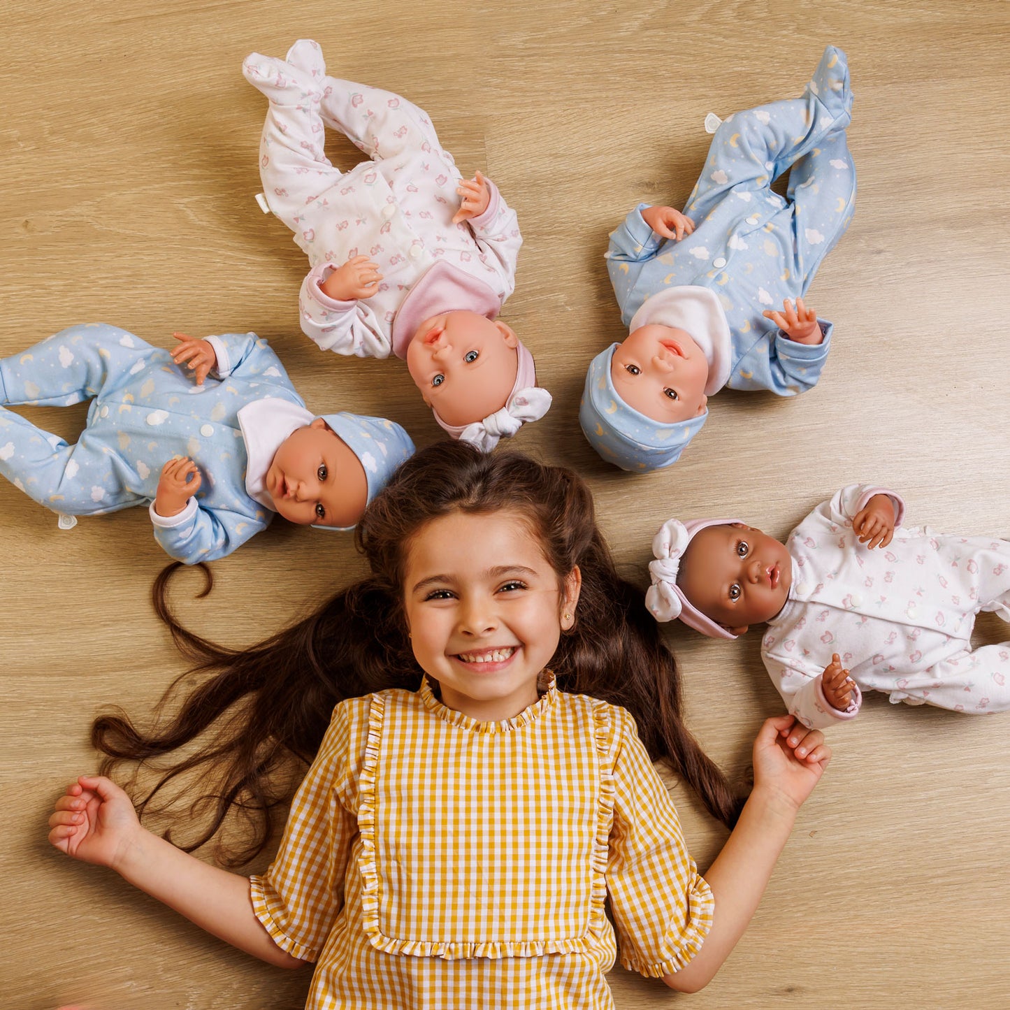 Young girl lying on a wooden floor with four baby dolls around her.