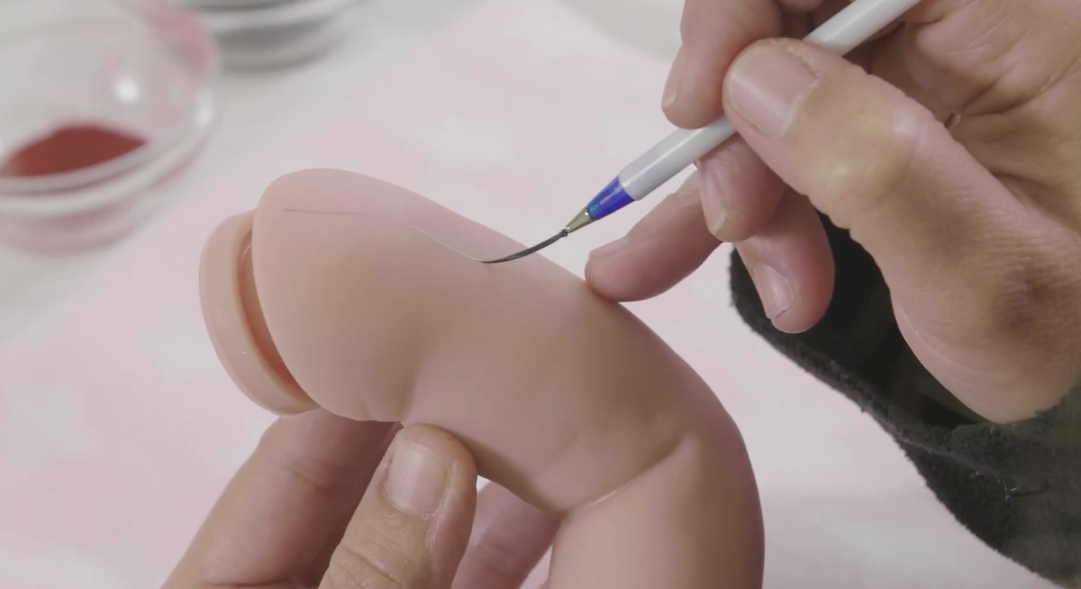 An artist hand painting a JC Toys reborn doll