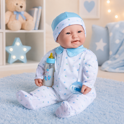 A baby doll or toy dressed in a light blue and white footed onesie with small blue floral prints, matching blue hat, and holding a bottle and pacifier, seated on a soft blue rug in a styled nursery setting.