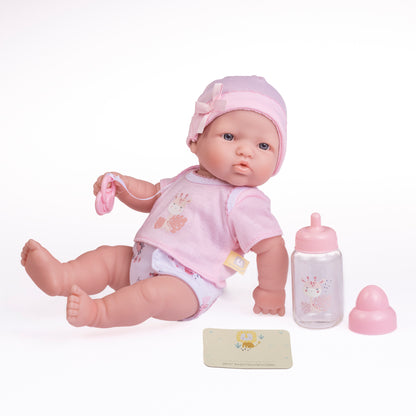 A 12-inch JC Toys La Newborn doll with soft vinyl skin, dressed in a pink outfit, accompanied by a bottle, pacifier, and birth certificate.