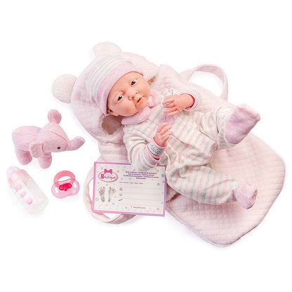 A soft body baby doll with a vinyl head, arms, and legs, dressed in a striped outfit, lying in a pink basket with a plush toy and accessories.