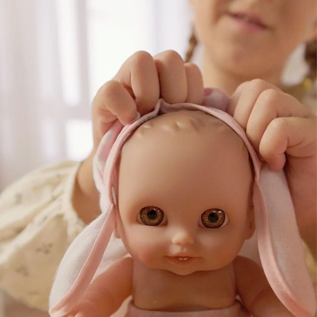Close-up of a child's hands putting a pink bunny-ear towel on a Lil' Cutesies baby doll's head.