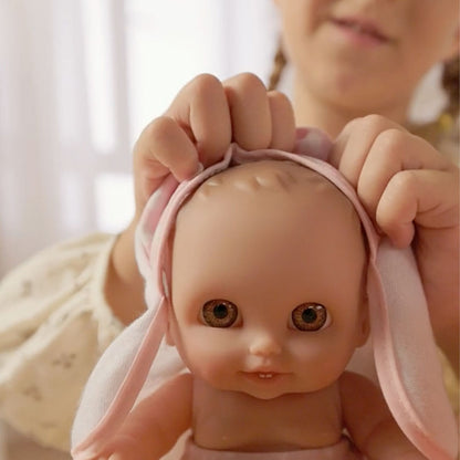 Close-up of a child's hands putting a pink bunny-ear towel on a Lil' Cutesies baby doll's head.