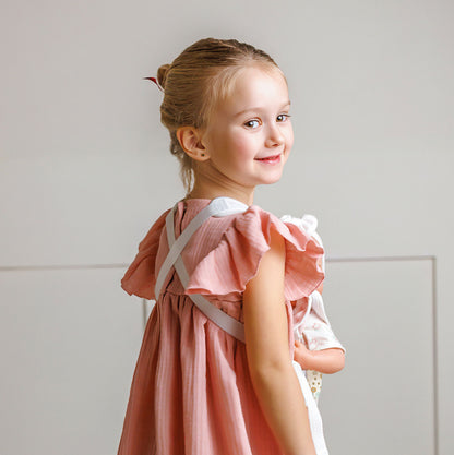 Young girl wearing a pink dress with ruffled sleeves against a light gray background