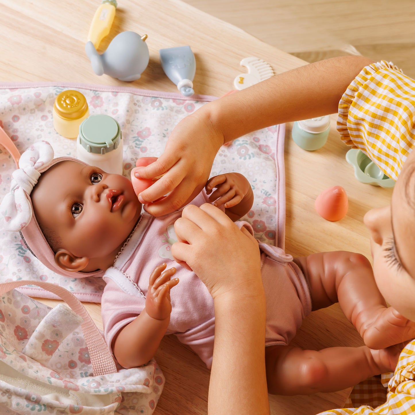 Baby doll being held by a child with toys on a wooden surface