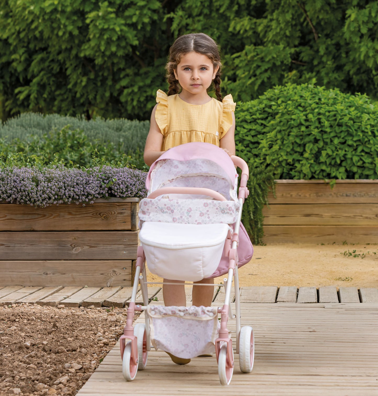 Young girl in a yellow dress pushing a pink stroller outdoors.