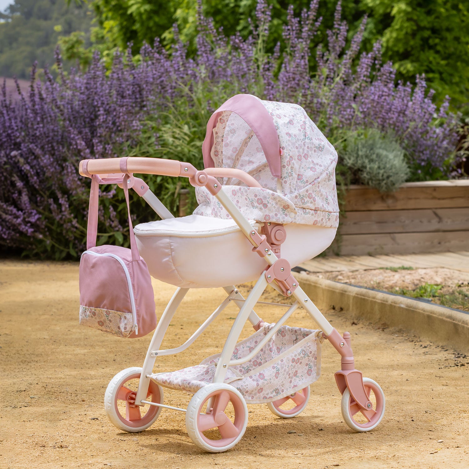 Pink and white floral pram with matching bag in a garden setting