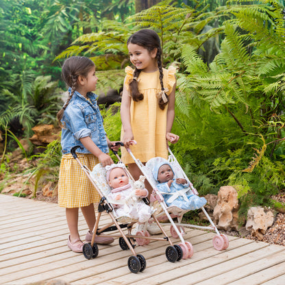 Two young girls with dolls in a stroller outdoors among greenery