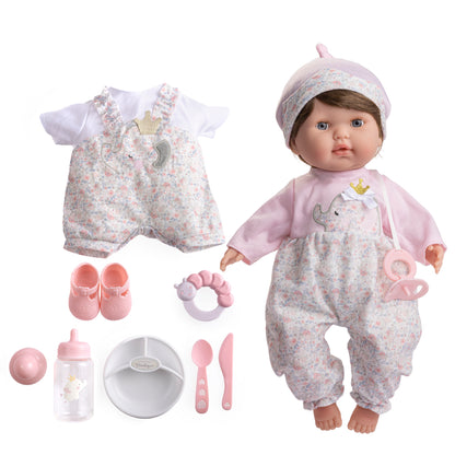 A realistic soft body baby doll with brown hair and open/close eyes, dressed in a pink outfit, accompanied by a two-piece embroidered outfit, shoes, a baby bottle, pacifier, rattle, and feeding accessories.