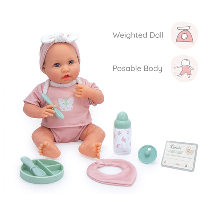 A baby doll play set featuring a weighted doll with a posable body, wearing a pink outfit and headband, sitting with a mint green toy spoon, a pink bib, a bottle, a small tray, and a card on a white background. Text callouts highlight the weighted doll and posable body features.