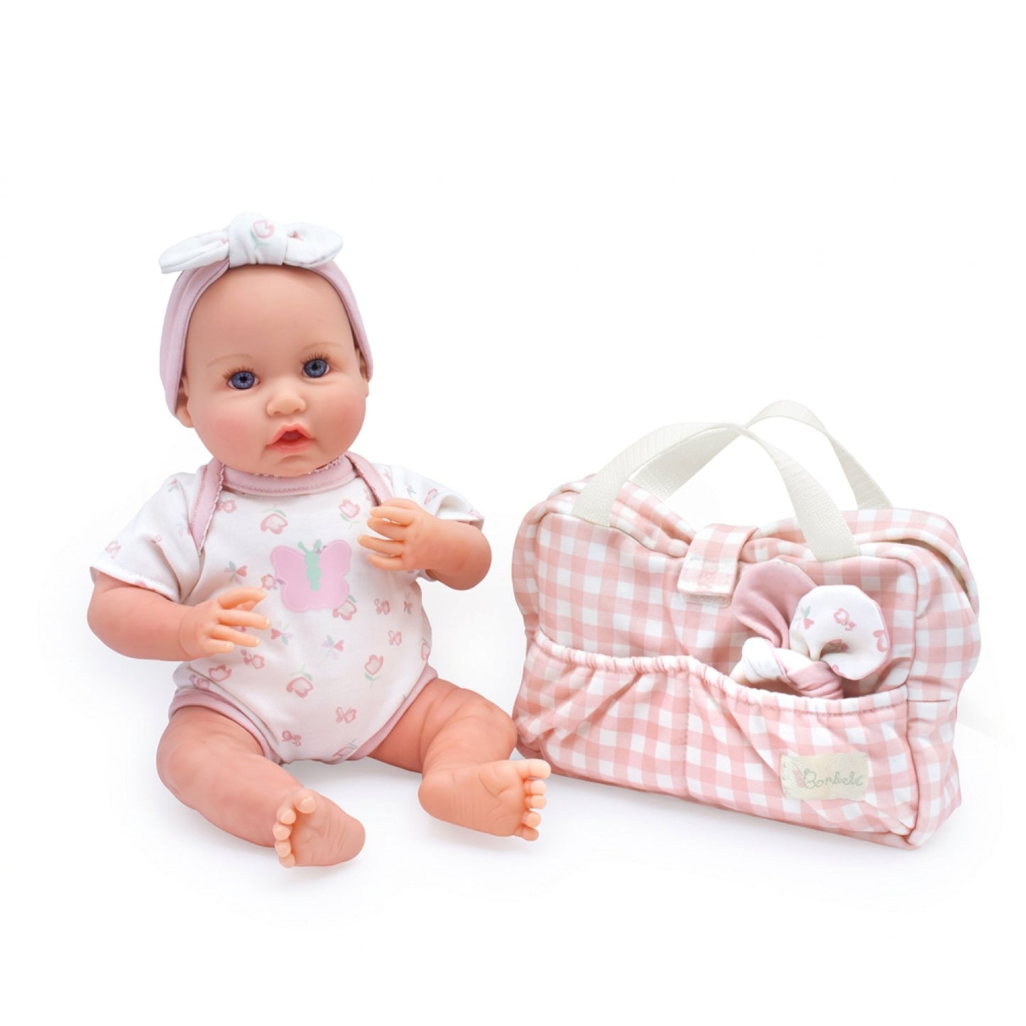 A baby doll with a pink bow headband and a white bunny-print bodysuit sits next to a matching pink-and-white gingham carrying bag with a small plush toy in the side pocket.