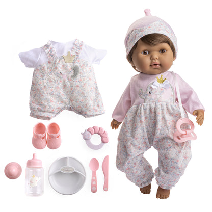 A realistic soft body baby doll with brown hair and closed eyes, wearing a pink outfit, accompanied by a pacifier, bottle, rattle, and feeding accessories.